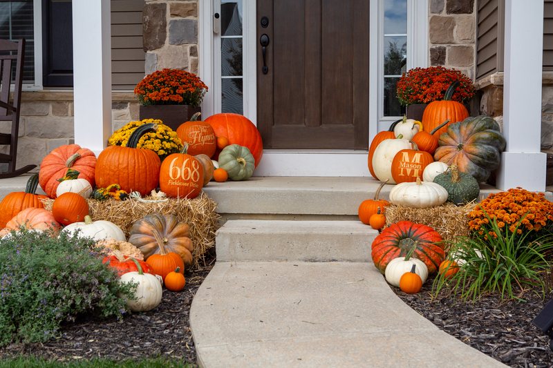 The Estate at step level, both pumpkin clusters flanking the door on straw bales, a family-name pumpkin, a house number and a Mason pumpkin among them