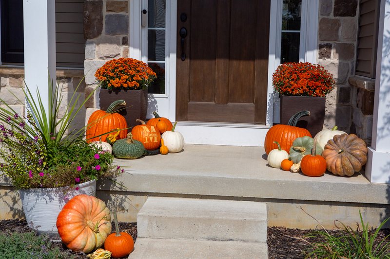 The Signature Porch at step level, both pumpkin clusters flanking the door, the engraved pumpkin among them
