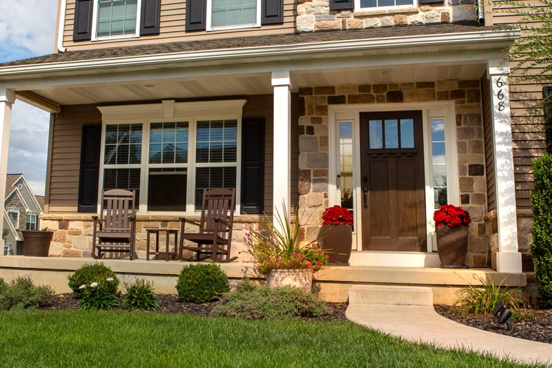 The same stone-front colonial porch before the pumpkins arrived, two rocking chairs on the deck
